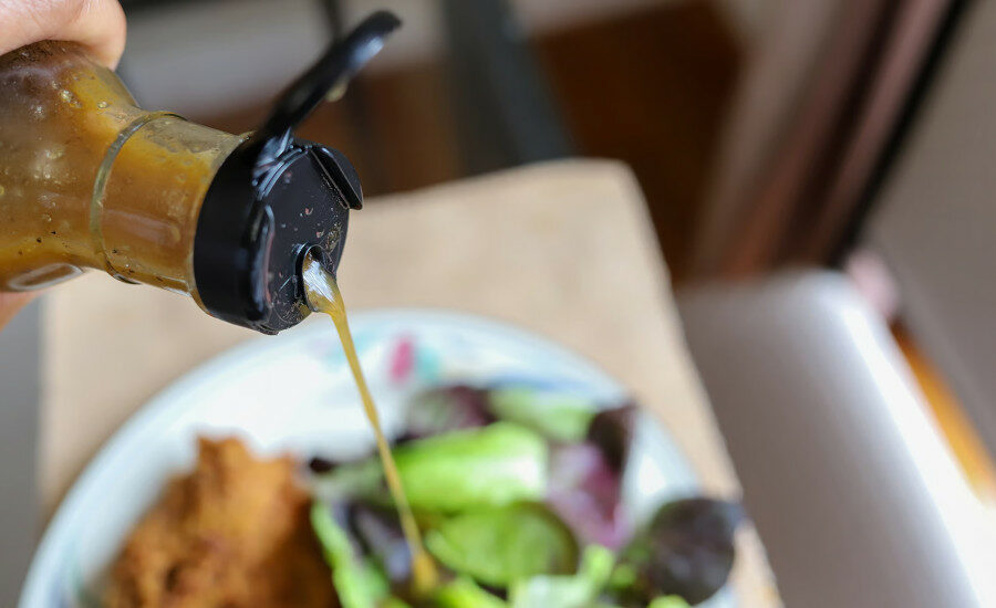 Bottle of Dressing Being Poured onto Salad